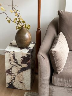 a marble block sitting next to a chair with a vase on it and a plant in the corner