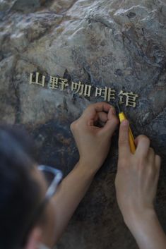 a person writing on a rock with chinese characters in the rocks behind them and another hand holding a pen