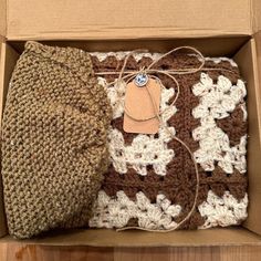 an open box with a brown and white crochet blanket in it, next to a hat