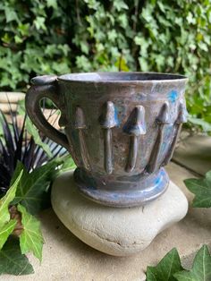 a cup sitting on top of a rock next to plants