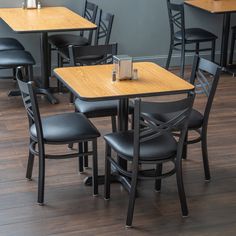 an empty restaurant with wooden tables and black leather chairs on hardwood flooring, in front of a gray wall