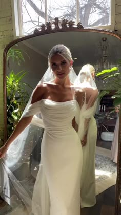 a woman in a wedding dress looking at herself in the mirror with her veil pulled back