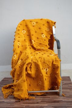 a chair covered with a yellow blanket on top of a wooden floor next to a wall