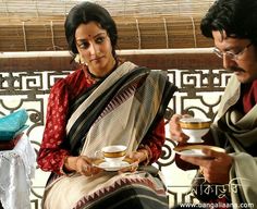 two women and a man sitting on a bench with cups of tea in their hands