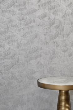 a round table with a gold base against a white wallpapered background that has wavy lines on it