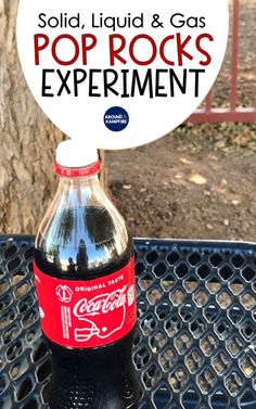 a bottle of soda sitting on top of a table next to a sign that says solid, liquid & gas pop rocks experiment