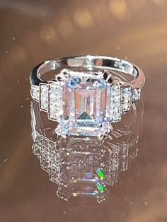 an emerald cut diamond ring on top of a shiny surface with reflection in the middle