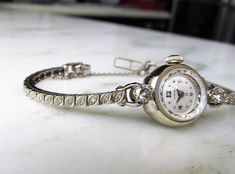 "This is a beautiful vintage Ladies Hamilton 14K white gold & diamond wrist watch. The round watch case is a 17mm size. The watch face is white with white gold Arabic 12, 3, 6, & 9. The other hours are marked with a dot. The watch features the original crown on the stem. The acrylic face has a faceted edge. The case is 14K white gold. It is marked Hamilton on the back. The inside of the case is marked Hamilton W Co. Lancaster PA, 14KT Gold, D75905, 817965. The movement is a 22 jewel adju Classic Diamond White Round Diamond Watch, Platinum Wedding Watch, Round, Wedding Platinum Watches, Round Shape, Platinum Diamond Watch For Wedding, Platinum Diamond Wedding Watch, Platinum Wedding Watch, Wedding Platinum Watches, Antique Round Watches With Diamond Hour Markers, Antique Watches With Diamond Hour Markers