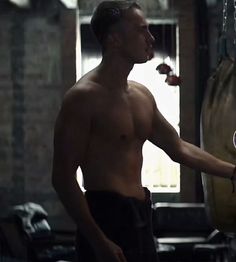 a shirtless man holding a tennis racquet in his right hand while standing next to a punching bag