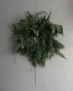 a wreath hanging on the wall with beads and greenery attached to it's sides