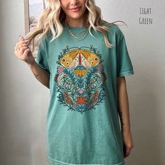 👀Images are an accurate depiction of what you'll receive upon purchase ♂️ All Shirts are Unisex Sizing 👣 Printing is "Direct To Garment"  (Ink printed). Step into a world of enchantment with our Mystical Moth T-shirt. This captivating piece of wearable art combines the timeless allure of folk art with the ethereal vibes of fairycore aesthetics. The graphic on this tee features a majestic moth, its wings adorned with intricate patterns reminiscent of ancient folk art. Surrounding the moth, a ce Casual Multicolor Vintage Print T-shirt, Green Casual Shirt With Vintage Print, Casual Green Shirt With Vintage Print, Green Vintage Print Short Sleeve Top, Green Vintage Print Tops For Summer, Green Tops With Vintage Print For Summer, Spring Vintage Print Top With Short Sleeves, Green Top With Vintage Print For Summer, Spring Top With Vintage Print And Short Sleeves