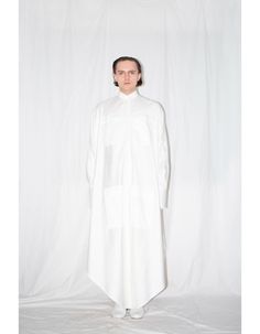 White zero waste cut elongated cloak shirt is bias-cut that ensures a voluminous silhouette and flattering fit. Constructed from 100% Italian cotton, the shirt features slim cut collar, front covered placket button closure, 4 patch pockets, buttoned side seam vents and elongated one button sleeve cuffs.FEATURES:- Elongated cloak shirt- 100% Italian cotton- Zero waste product- Side seam slits with buttons- Slim collar- Concealed front placket button closure- Bias cut- Styled here with our White A Oversized Asymmetrical Cotton Shirt, White Asymmetrical Cotton Shirt, Oversized White Shirt Dress With Pockets, Oversized Tunic With Shirttail Hem, White Workwear Shirt With Asymmetrical Hem, White Cotton Shirt With Asymmetrical Hem, White Asymmetrical Hem Shirt For Work, White Shirt With Asymmetrical Hem For Work, White Oversized Long Sleeve Tunic