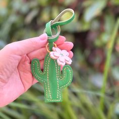 a hand holding a green key chain with a flower on it and a cactus charm