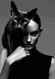 a black and white photo of a woman with a cat on her head, in front of a gray background