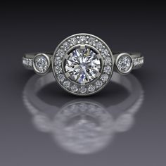 "A round brilliant cut half carat lab grown diamond in a 6-prong head is surrounded by a halo of diamonds and flanked by bezel-set diamonds in this 14k white gold engagement ring. The top of the ring measures about 9.8mm at the widest point. Matching band available; price on request. Diamond Dimensions5mm (approx) Carat Weight .50 (approx) Enhancement Lab Created ColorE-F ClarityVS2 CutExcellent PolishExcellent Diamonds Number        32 EnhancementNatural Carat Total Weight0.45 ColorF-G ClaritySI1-2 Cut        Very Good PolishVery Good This is a custom made item! When you order, we will create a wax model of your ring with our 3D printer. This model is then cast in 14k gold, which is polished and set by hand. This process takes 3-4 weeks, so please allow for this time when ordering if your Three Stone Halo Engagement Ring, Engagement Ring With Bezel, Three Stone Engagement Rings Halo, Amethyst And Diamond Ring, White Gold Engagement Ring, Bezel Set Diamond, Three Stone Engagement, Three Stone Engagement Rings, White Gold Engagement