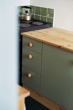 a kitchen with green cabinets and a tea kettle sitting on the stove top next to it