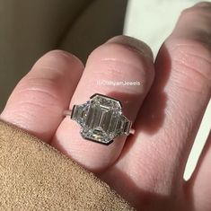 a close up of a person's hand holding an engagement ring with a diamond in it