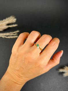 a woman's hand with a gold ring and green stone on it, next to some feathers