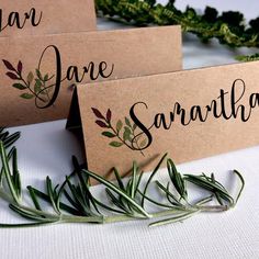 three place cards with herbs on them sitting next to some greenery and twine