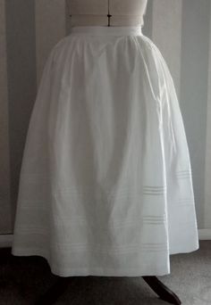 The Romantic silhouette saw the advent of the bell-shaped skirt, not so wide or extravagant as the later 1850s crinoline would be, but nevertheless requiring petticoats to create the fashionable silhouette. These petticoats could be tucked or corded and were frequently starched to increase their volume.   This delightful replica is based on 1830s originals, is ideal for wearing over a corded petticoat, and features  three groups of tucks to hold out the hemline. It is made from 100% cotton, Oeko Fitted Daywear Petticoat With Full Skirt, Fitted Full Skirt Petticoat For Daywear, Vintage Costume Gathered Skirt, Vintage Gathered Skirt For Costume, Vintage Full Skirt Petticoat For Costume, Vintage Voluminous Full Skirt Petticoat, White Vintage Crinoline Petticoat, Fitted Vintage Flared Petticoat, Vintage Full Voluminous Petticoat