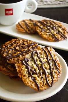 two cookies with chocolate drizzled on them sitting on white plates next to a cup of coffee