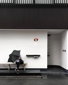 a person sitting on a bench with an umbrella in front of a white wall and black stairs