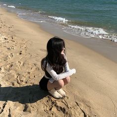 a woman sitting on the beach with her legs crossed looking out at the water and sand