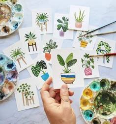 a person holding up some cards with plants on them next to paintbrushes and paints