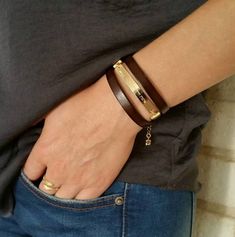 a woman wearing a brown leather bracelet with a gold plated clasp on her wrist