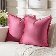 two pink pillows sitting on top of a white couch next to a potted plant