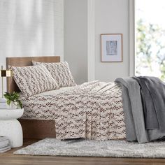 a bed sitting next to a window covered in blankets and pillows on top of a rug