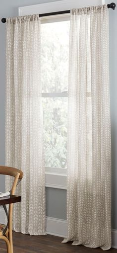 a white curtain hanging on the side of a window next to a chair and table