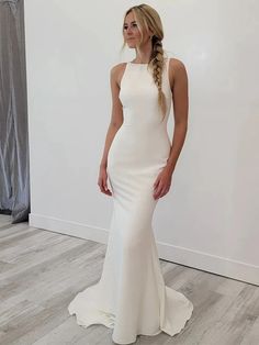 a woman standing in front of a white wall wearing a long white dress and braid