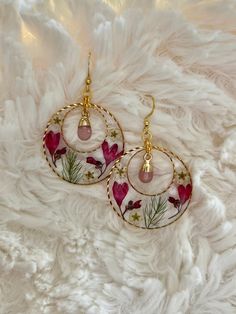 a pair of earrings with pink flowers and gold accents on a white furnishing