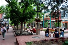 people are sitting on benches in the middle of a city street with shops and trees