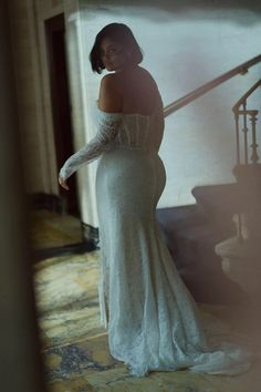 a woman in a white dress standing next to a stair case and looking off into the distance