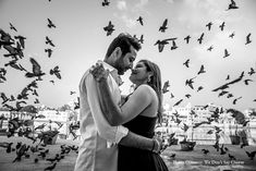 a man and woman standing next to each other with birds in the air behind them