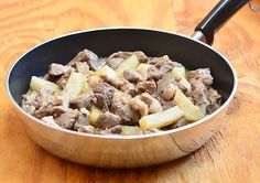 a pan filled with meat and potatoes on top of a wooden table