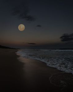 the moon is setting over the ocean with waves coming up to it's shore