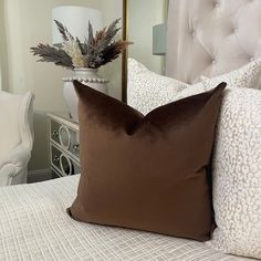 a brown pillow sitting on top of a bed next to a vase with flowers in it