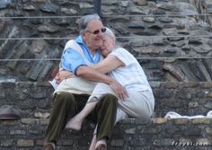 an older man and woman are sitting on some steps together, hugging each other with their arms around each other