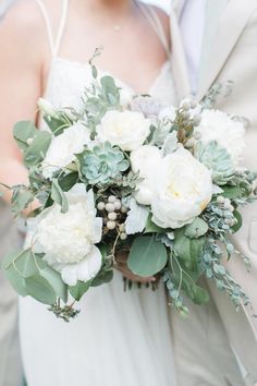 a bride holding a bouquet of white flowers and greenery