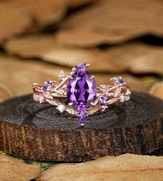 an amethorate ring sitting on top of a piece of wood with leaves around it