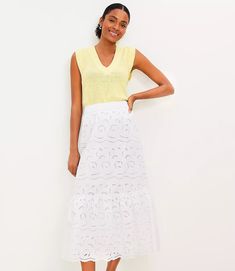 a woman in a yellow top and white skirt posing for the camera with her hands on her hips