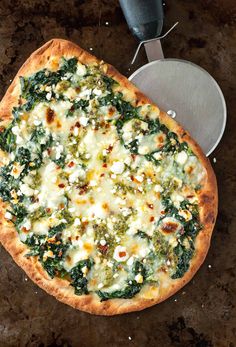 a pizza with cheese, spinach and other toppings on it next to a spatula