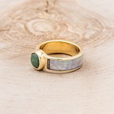 a gold ring with a green stone in the middle on top of a piece of wood