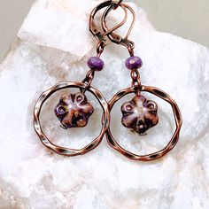 Purple glass flowers floating inside twisted copper rings make these Boho dangle earrings extra special. Copper rings frame the flower beads that have shades of purple, lavender and a Picasso finish.  Lightweight and versatile, these cute earrings will add a pop of color and sophistication to your look.  Custom ear wire style choice at checkout. Hypoallergenic ear wires (nickel and lead free).  Free gift packaging included. Earrings are carded and in an organza bag. Artisan glass beads produced Unique Copper Flower Jewelry, Unique Metal Flower Jewelry, Unique Flower Shaped Metal Jewelry, Nickel-free Copper Artsy Jewelry, Unique Flower-shaped Metal Jewelry, Artsy Nickel-free Copper Jewelry, Whimsical Czech Glass Jewelry With Ear Wire, Whimsical Czech Glass Jewelry Set With Earrings, Artsy Copper Drop Earrings