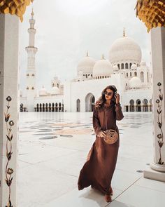 a woman standing in front of a white building talking on a cell phone while wearing a brown dress