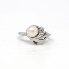 "Timeless vintage 10k white gold cultured pearl ring with a diamond accent! This classic piece features a genuine white cultured pearl accented by a round cut diamond weighing an estimated 0.02 carats. The ring has an asymmetrical design with a modern leaf-life design surrounding the pearl. The tiny sparkling diamond is securely set in prongs. Stunning retro piece of fine jewelry showcasing June's birthstone, circa 1950s! ERA - Circa 1950s, Mid Century MARKINGS / MATERIAL - 10k white gold, genui Classic Brilliant Cut Diamond White Pearl Ring, Classic Pearl Ring With Prong Setting In Diamond White, Classic Pearl Ring With Prong Setting, Classic Diamond White Pearl Ring With Prong Setting, Classic White Gold Pearl Ring With Diamond Accents, Classic Pearl Ring With Diamond Accents For Anniversary, Classic Pearl Ring With Brilliant Cut, Classic White Gold Pearl Ring With Prong Setting, Vintage White Pearl Ring With Brilliant Cut