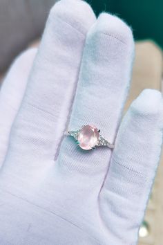 a person's hand with a pink ring on top of their finger and white gloves